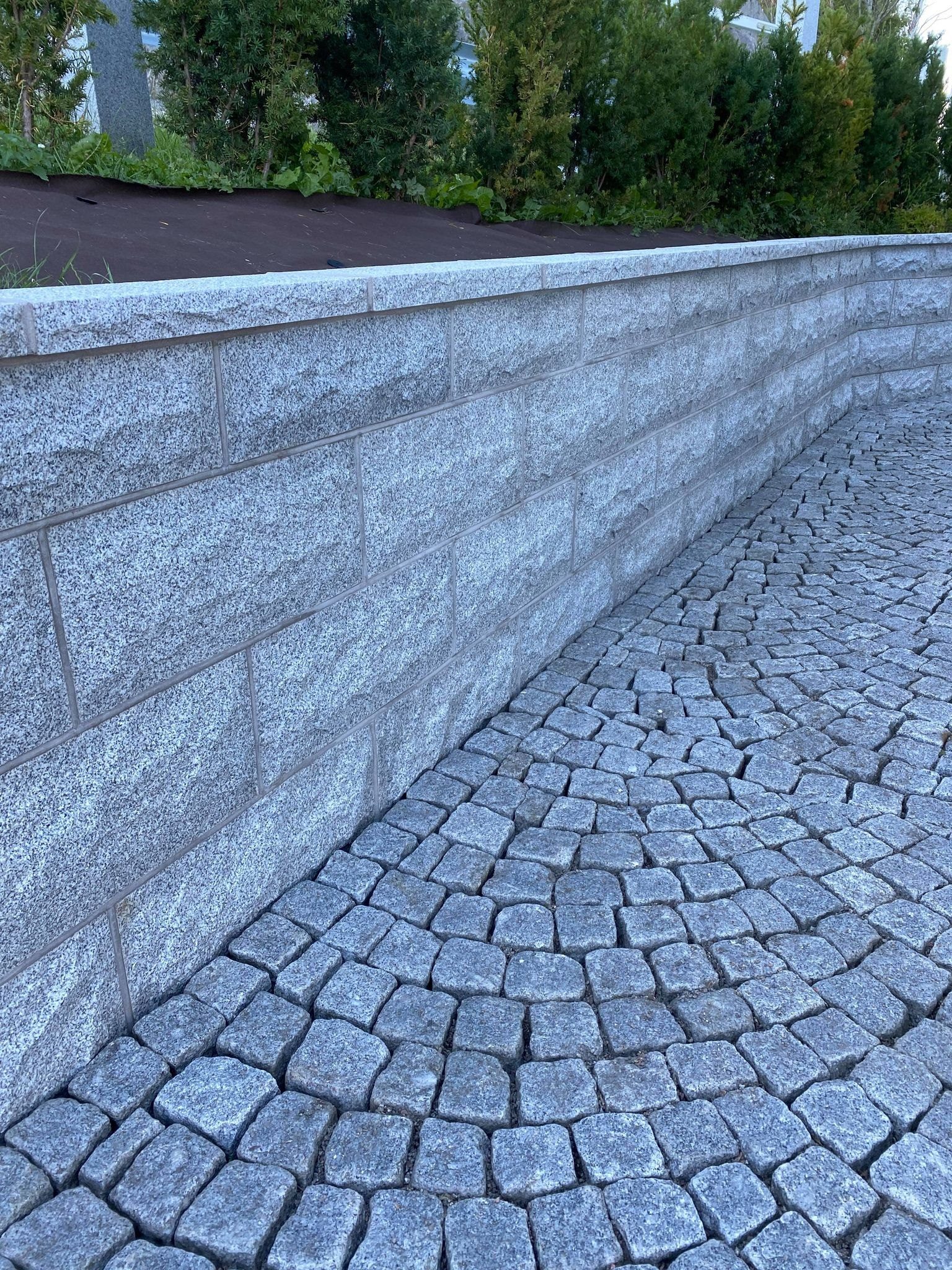 Curved granite retaining wall beside cobblestone paving